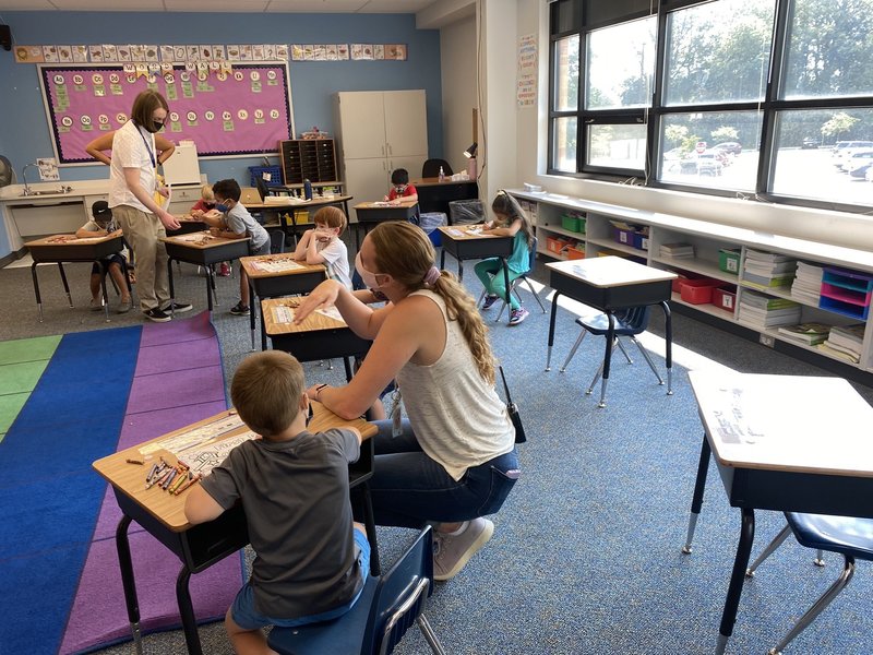 Two teachers helping students at their desks finish a coloring activity.