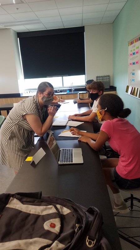 A student at a desk with her laptop open talking with her teacher.