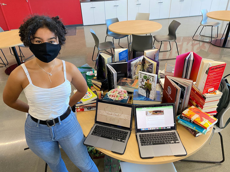 Young lady with two computers registering students for the Meridian Book Club in front of several books being displayed on a table.
