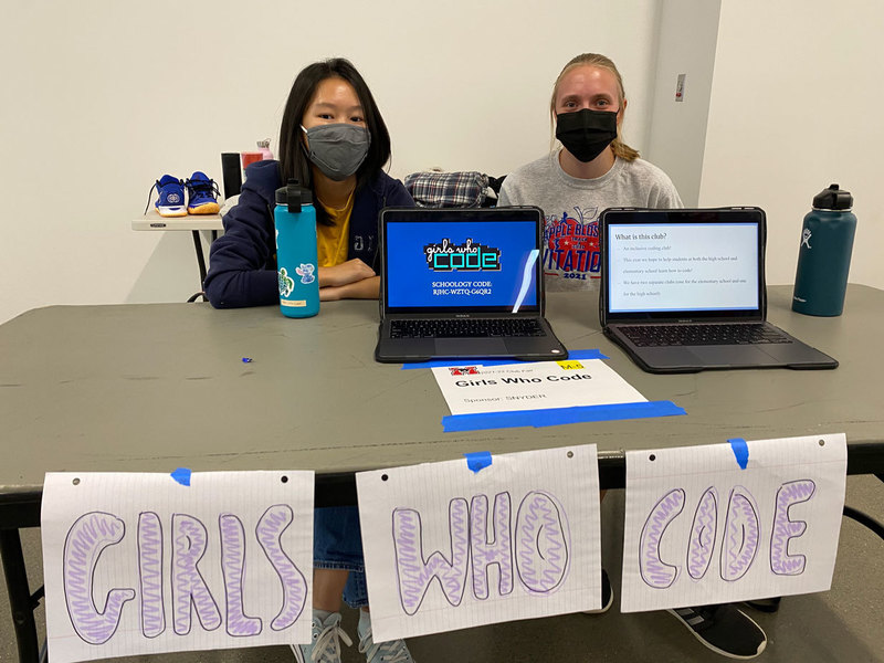 Two female students sitting at computers registering students for the Girls Who Code club.