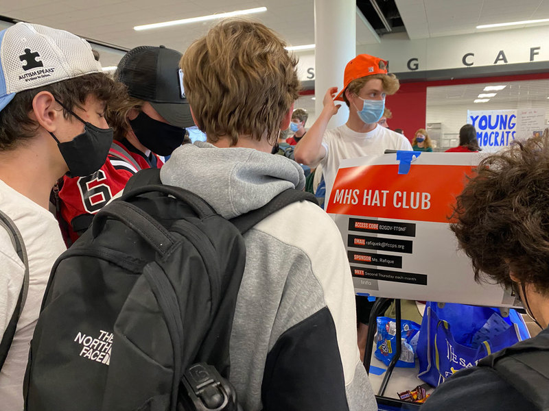 A group of boys looking at a poster explaining the Meridian Hat Club