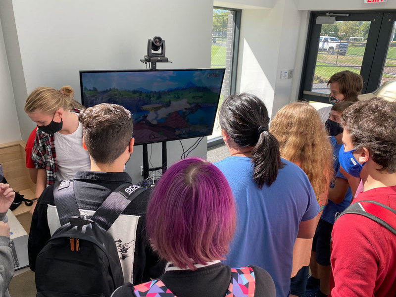 A group of students watching one student playing a video game on a large screen demonstrating the Meridian Role-Playing Club